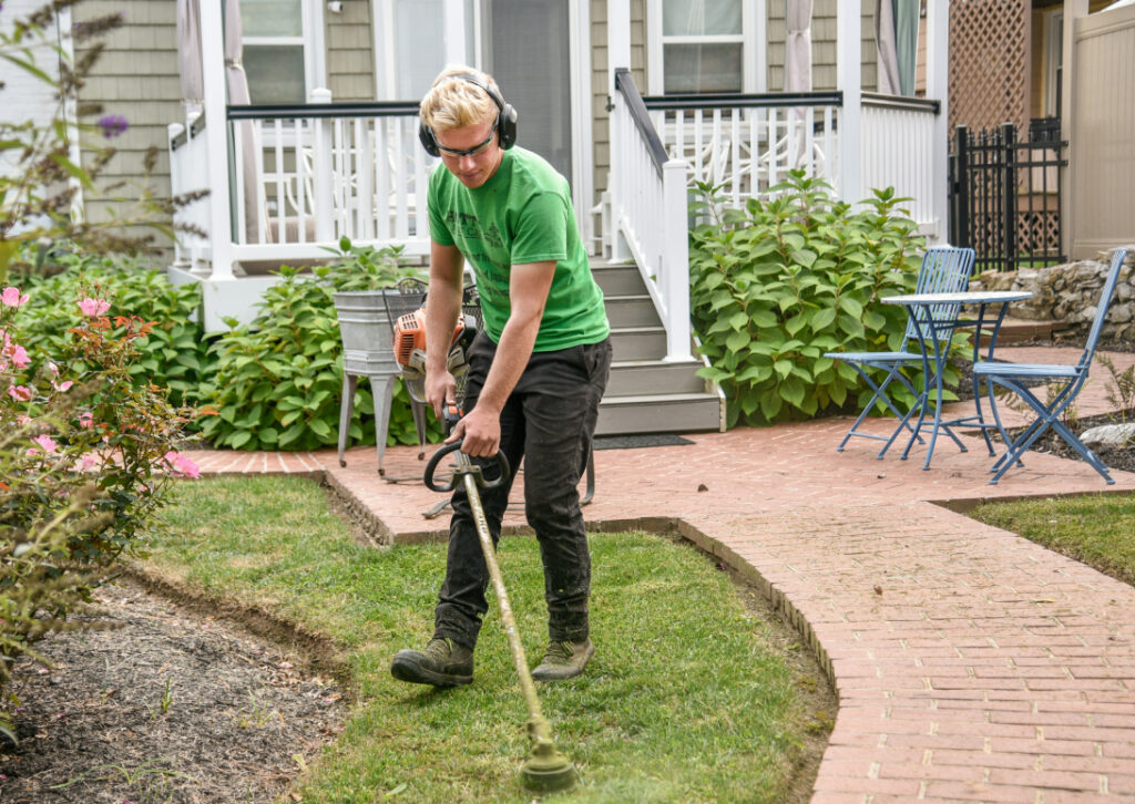 Man in green shirt mowing grass at the front yard of a house