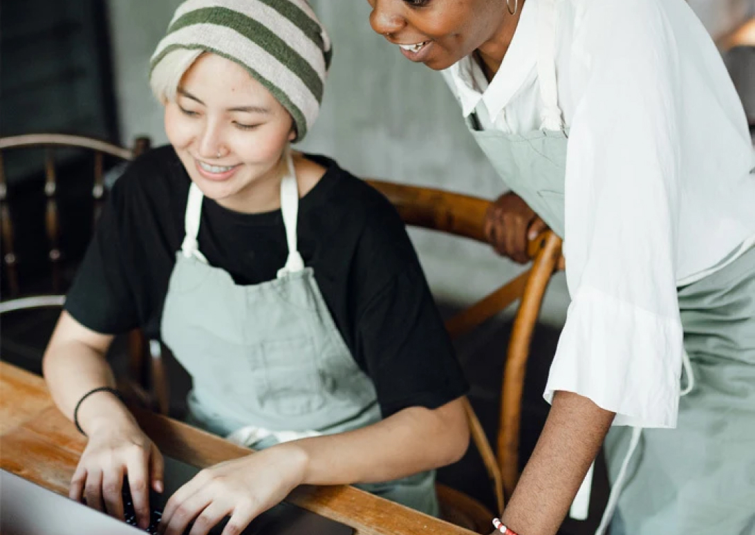 2 workers in aprons working in front of a laptop